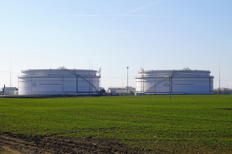 Large white cylindrical petrochemical storage tanks in a green field under clear blue sky