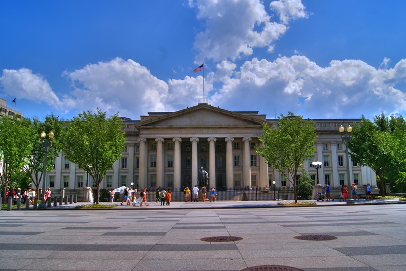 The neoclassical facade of the U.S. Treasury Building in Washington, D.C., with columns and an American flag atop