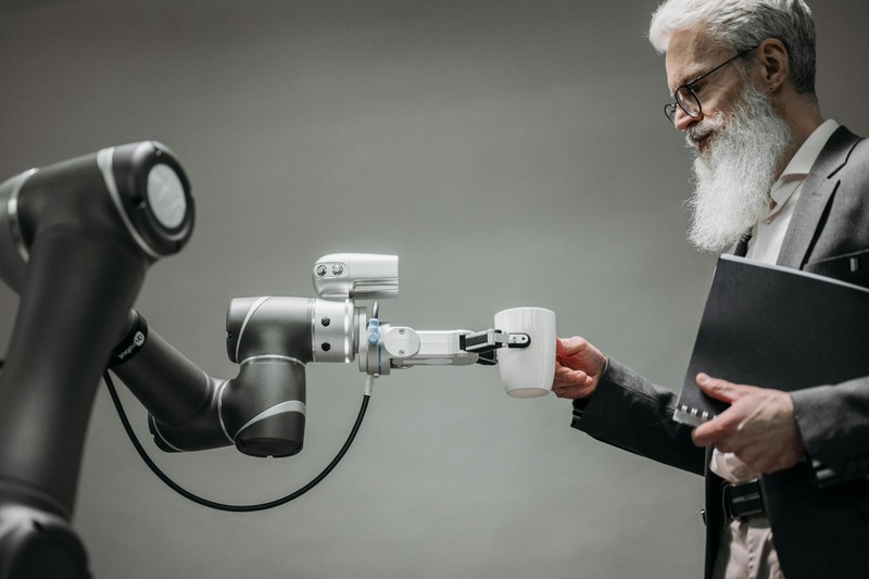 An older man in a suit interacts with a robotic arm in an office setting