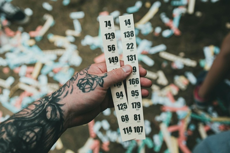 A hand holding numbered raffle tickets scattered on the ground