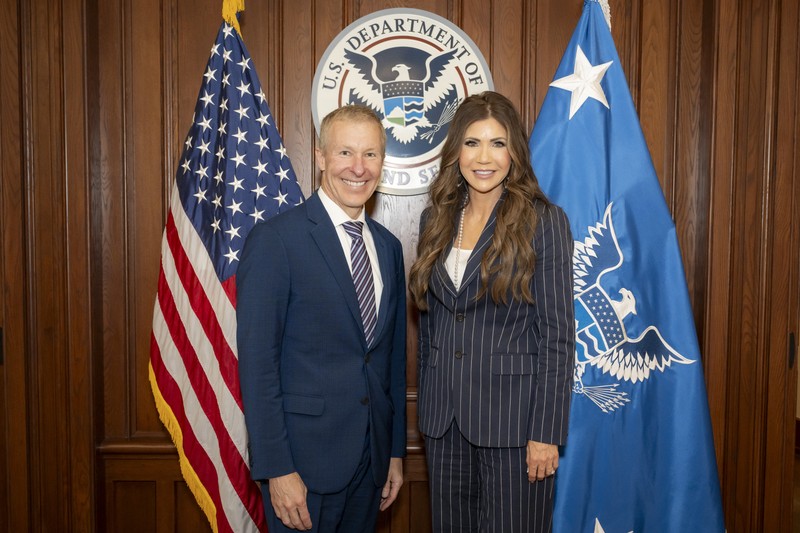 Scott Kirby, CEO of United Airlines, poses with DHS Secretary Kristi Noem in front of U.S. and Homeland Security flags at DHS Headquarters.