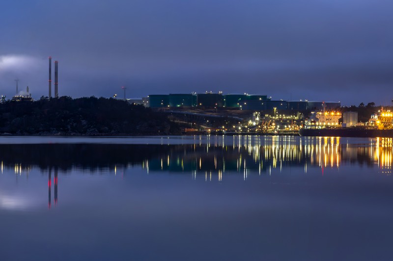 Oil refinery at blue hour with fog rolling over towers and calm waterfront reflections