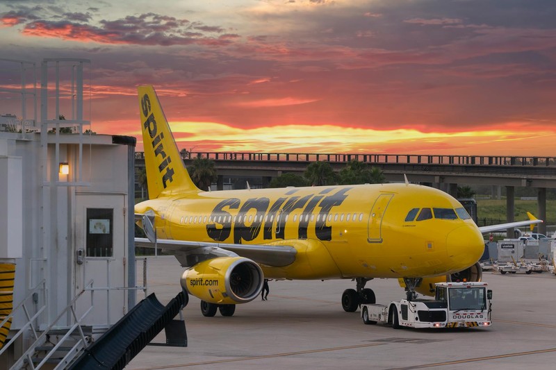 A bright yellow Spirit Airlines plane parked at an airport gate during a vivid sunset
