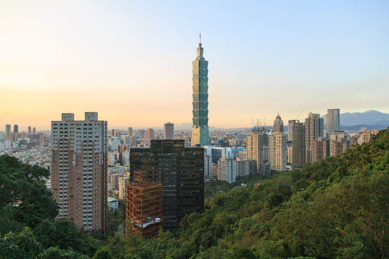 Taipei 101 tower rising above the Taipei city skyline at golden hour, framed by lush greenery
