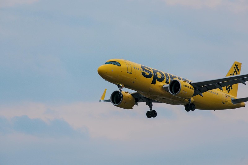 A bright yellow Spirit Airlines jet flying through a partly cloudy blue sky