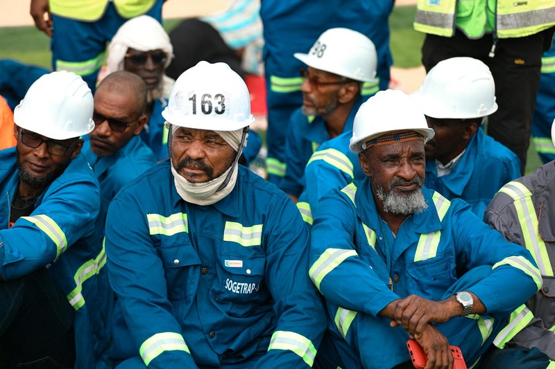 Construction workers in blue uniforms and white hard hats resting together outdoors at a job site