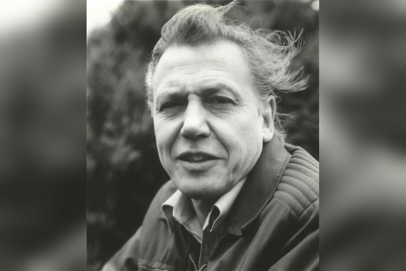 Sir David Attenborough in an outdoor setting, wind blowing through his hair, wearing a quilted jacket