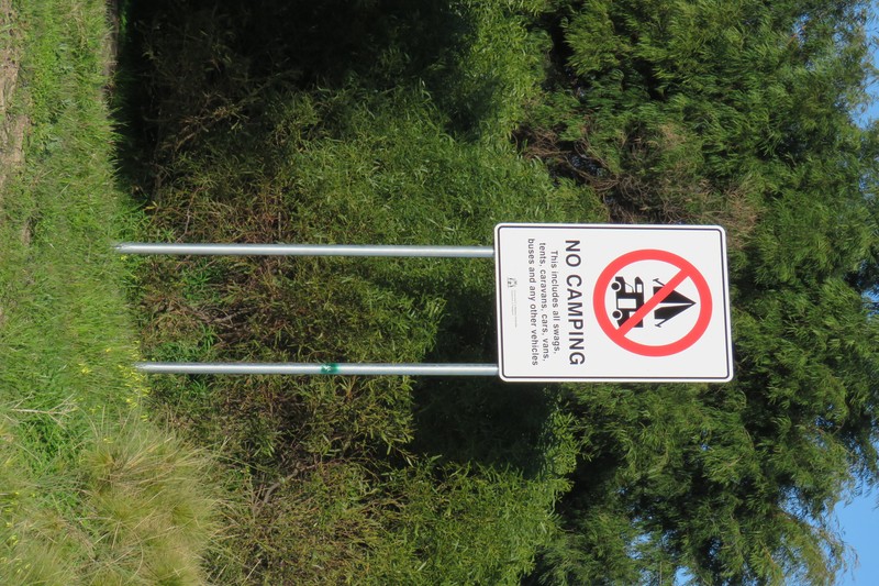 A 'No Camping' sign on Rockingham Beach, Western Australia, surrounded by bushland