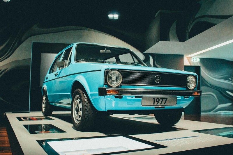 A light blue 1977 Volkswagen Golf Mk1 displayed in a modern automotive museum exhibition