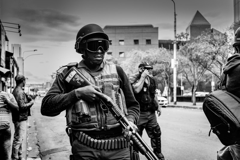Armed security forces in tactical gear patrol a South African urban street as civilians look on