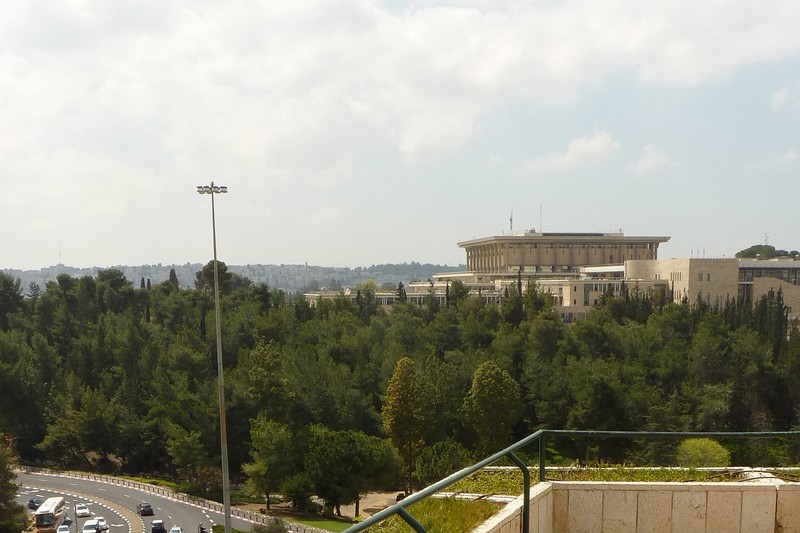 The Knesset building in Jerusalem viewed from an elevated vantage point, surrounded by greenery