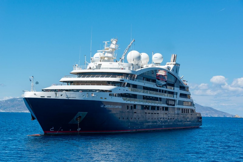 A sleek cruise ship sailing on calm blue waters with distant mountains on the horizon